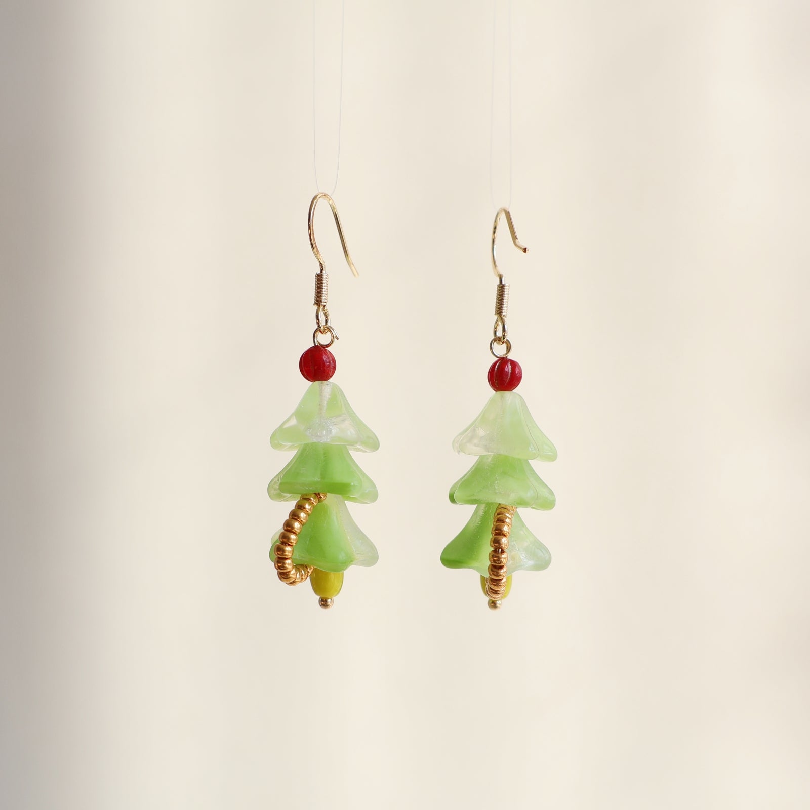 Green tree-shaped earrings with red and gold accents on a beige background