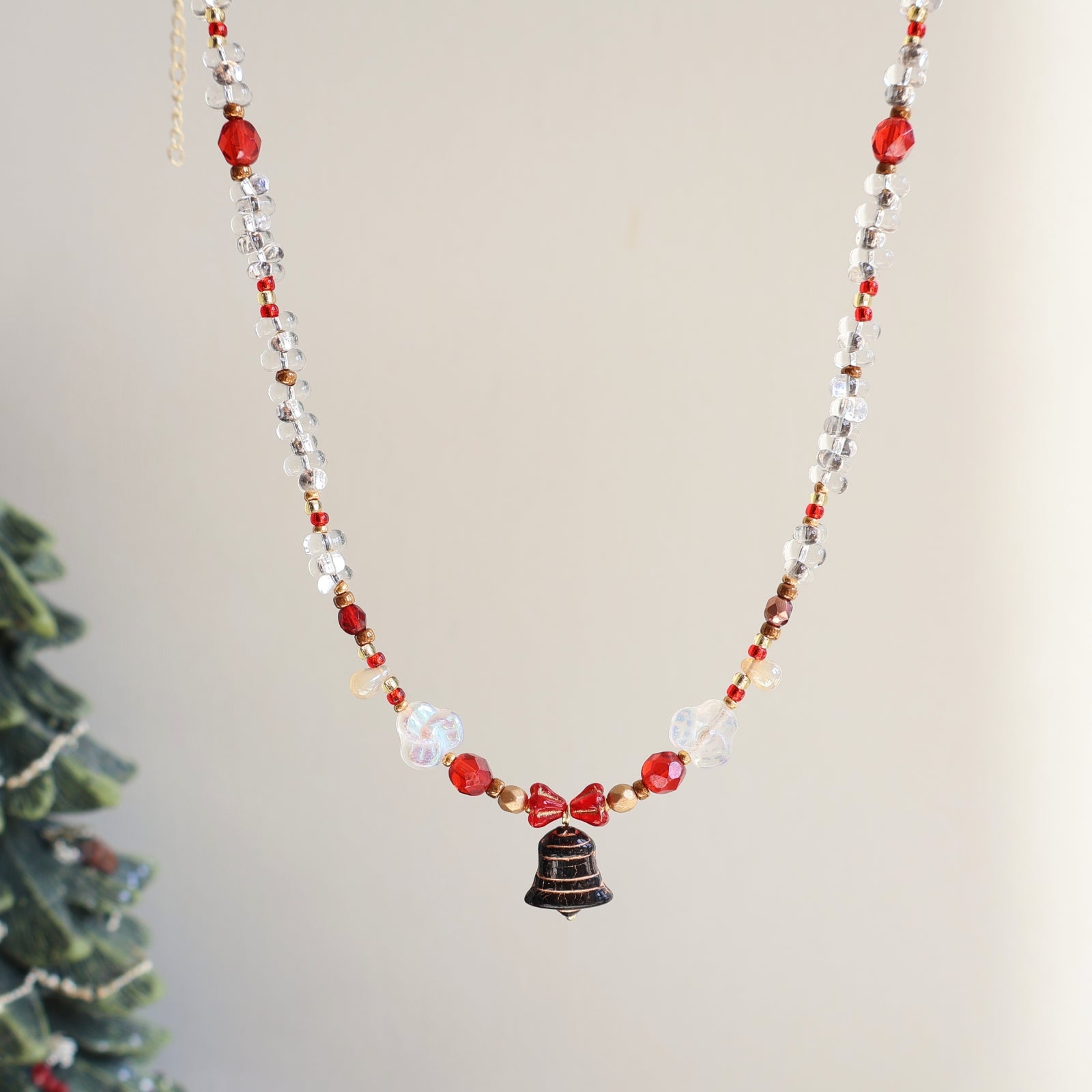 Necklace with red and clear beads and a bell charm on a neutral background