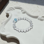Clear bracelet with a blue bead on a white ceramic dish