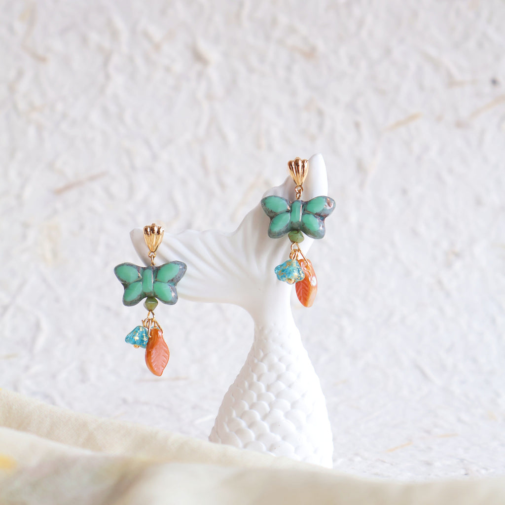 Butterfly-shaped earrings with turquoise and orange stones on a textured white surface