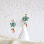 Butterfly-shaped earrings with turquoise and orange stones on a textured white surface