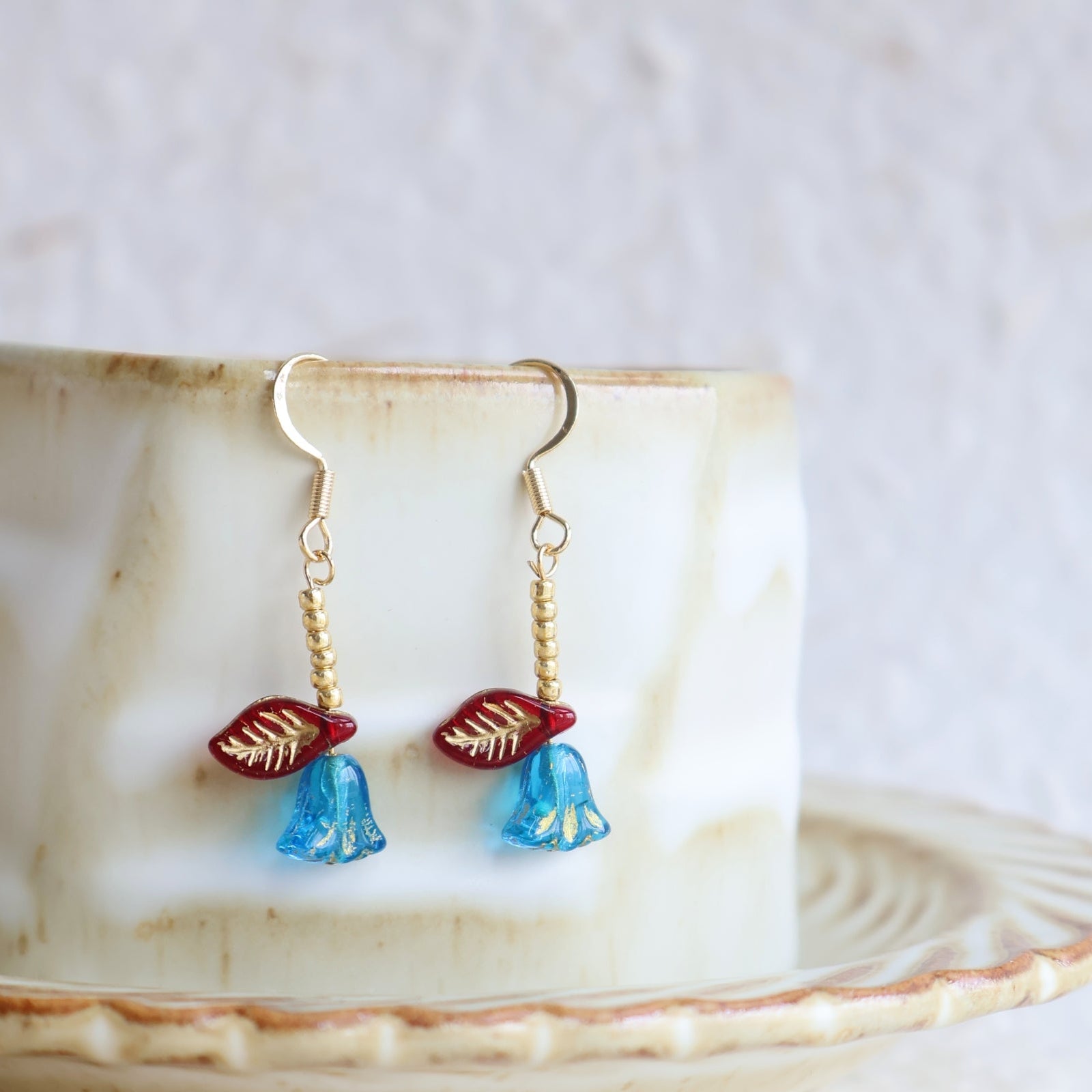 Pair of earrings with blue and red accents on a ceramic plate.
