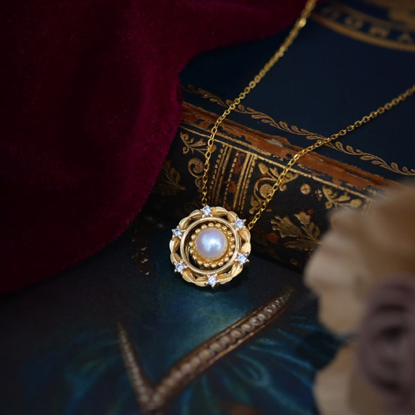 Gold necklace with a pendant featuring a pearl on an ornate book