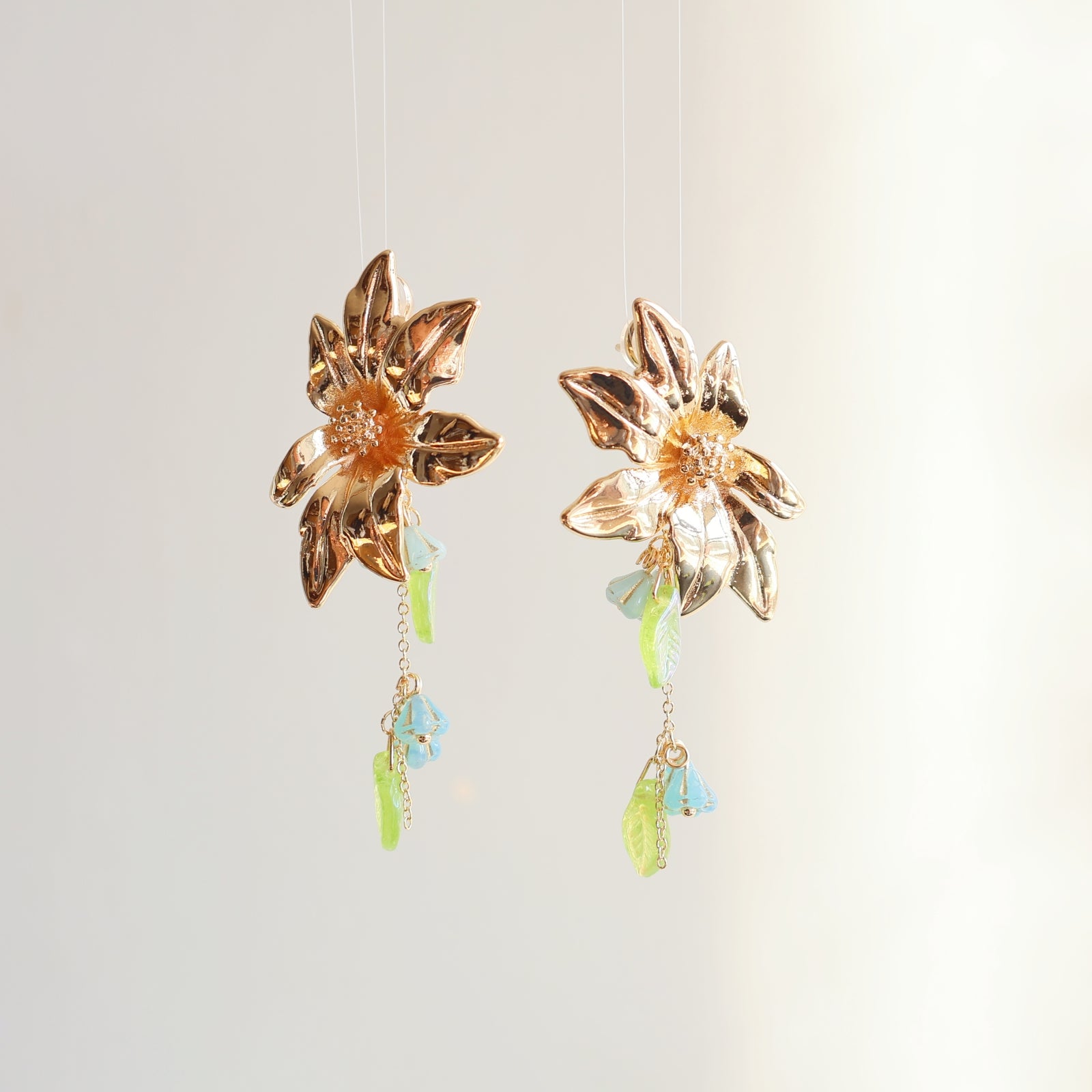 Gold flower-shaped earrings with colorful beads on a light gray background