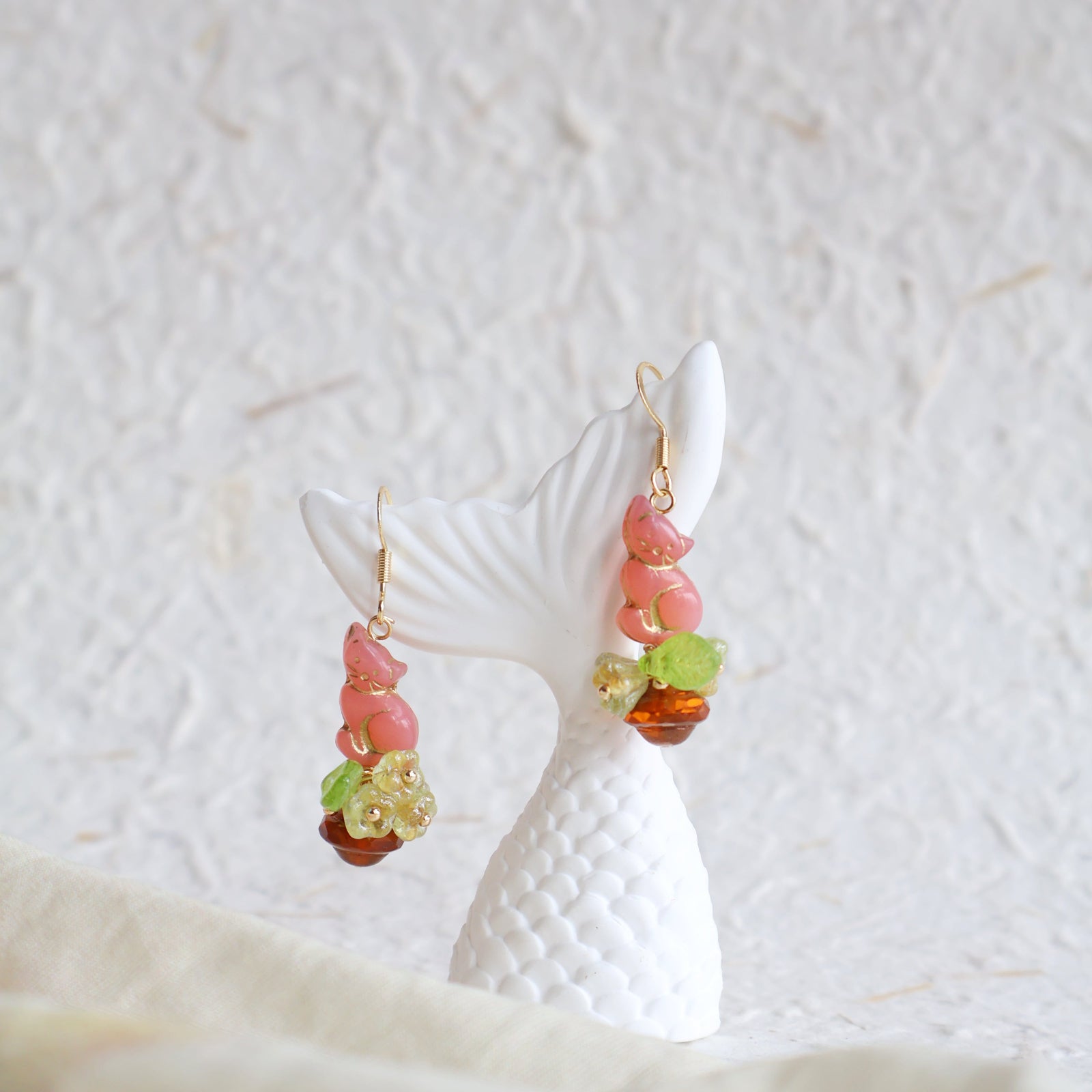 Colorful beaded earrings on a white ceramic stand against a textured white background