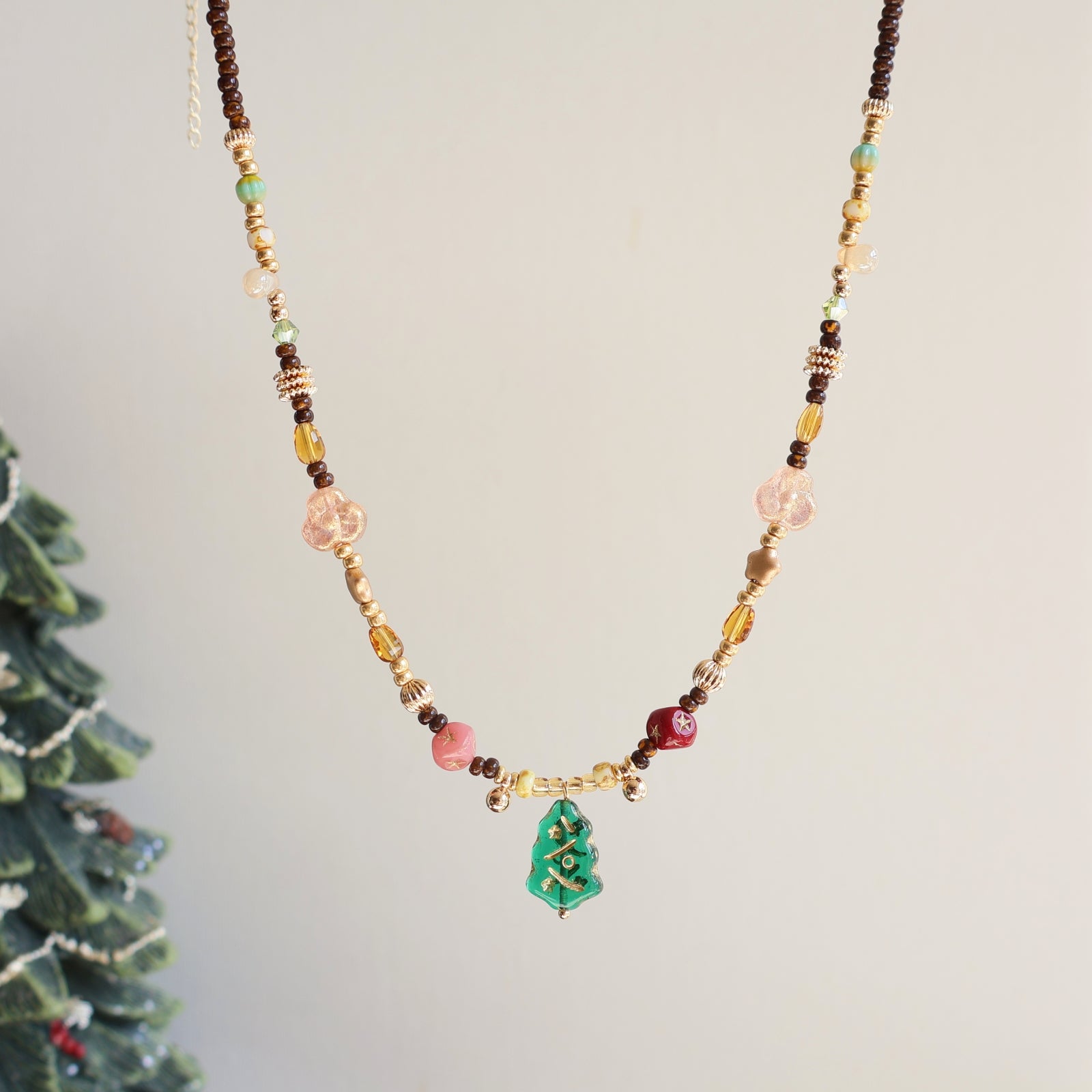 Necklace with beads and a small green tree charm against a neutral background