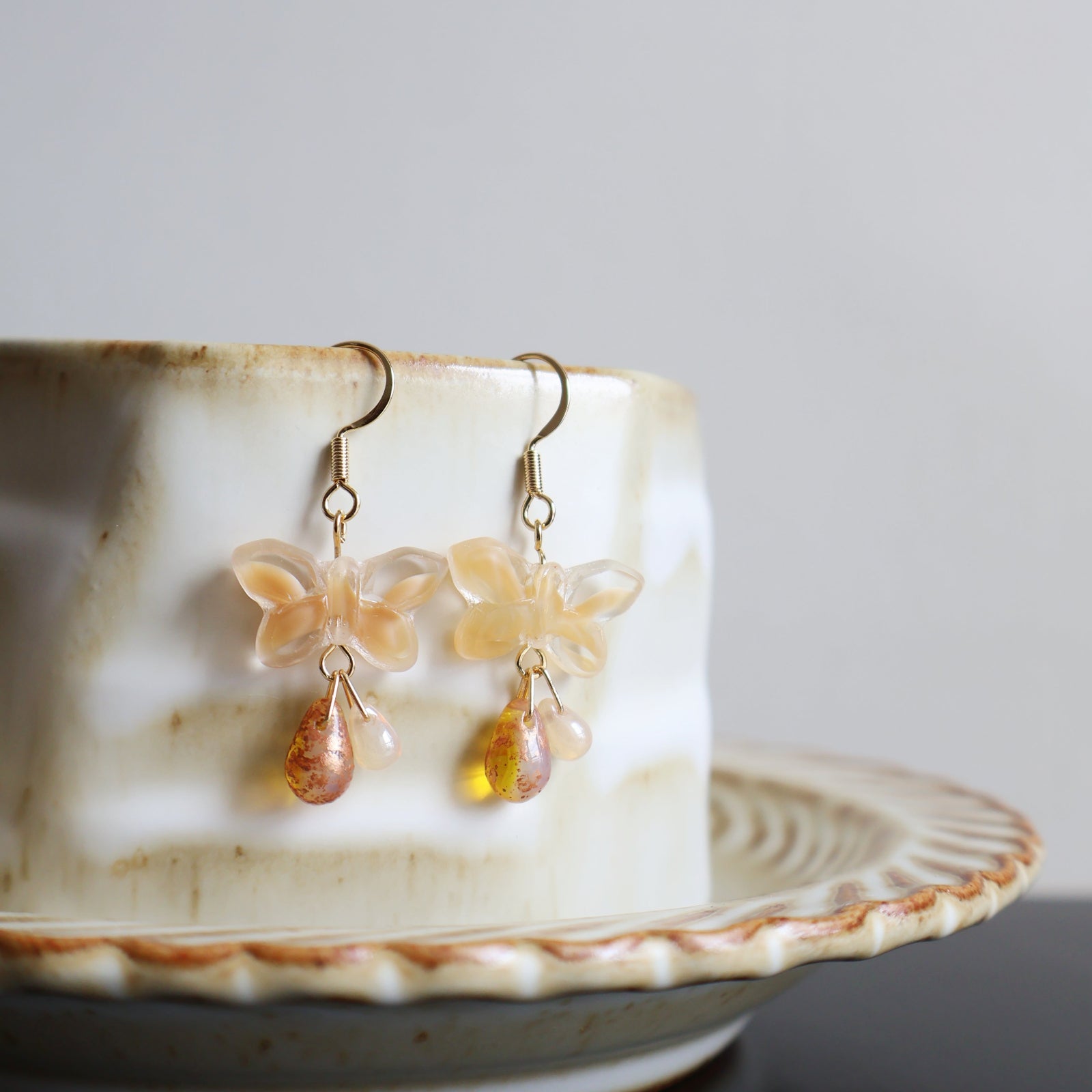 Butterfly-shaped earrings with gold accents on a ceramic dish.