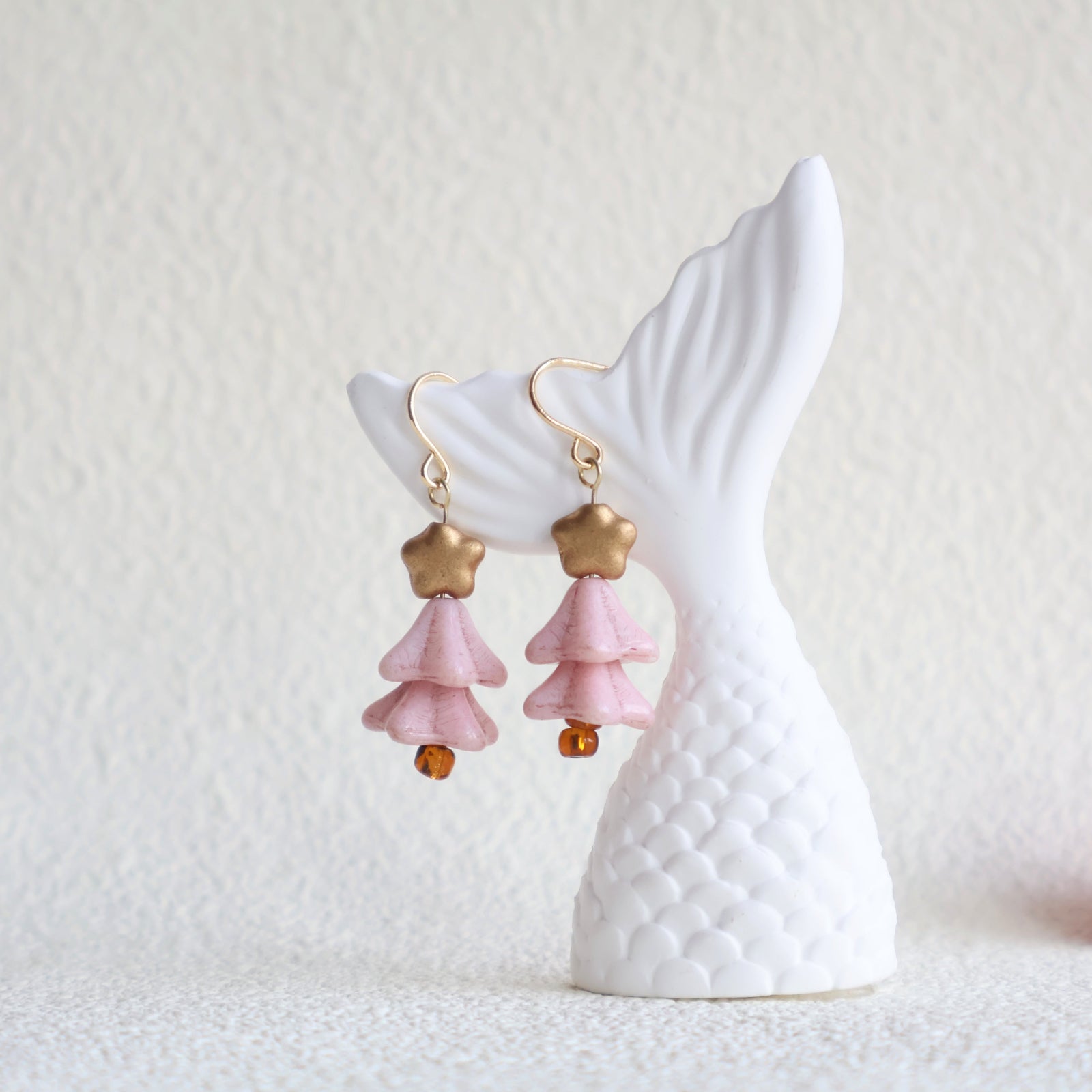 Pink and gold earrings on a white ceramic stand with a textured white background