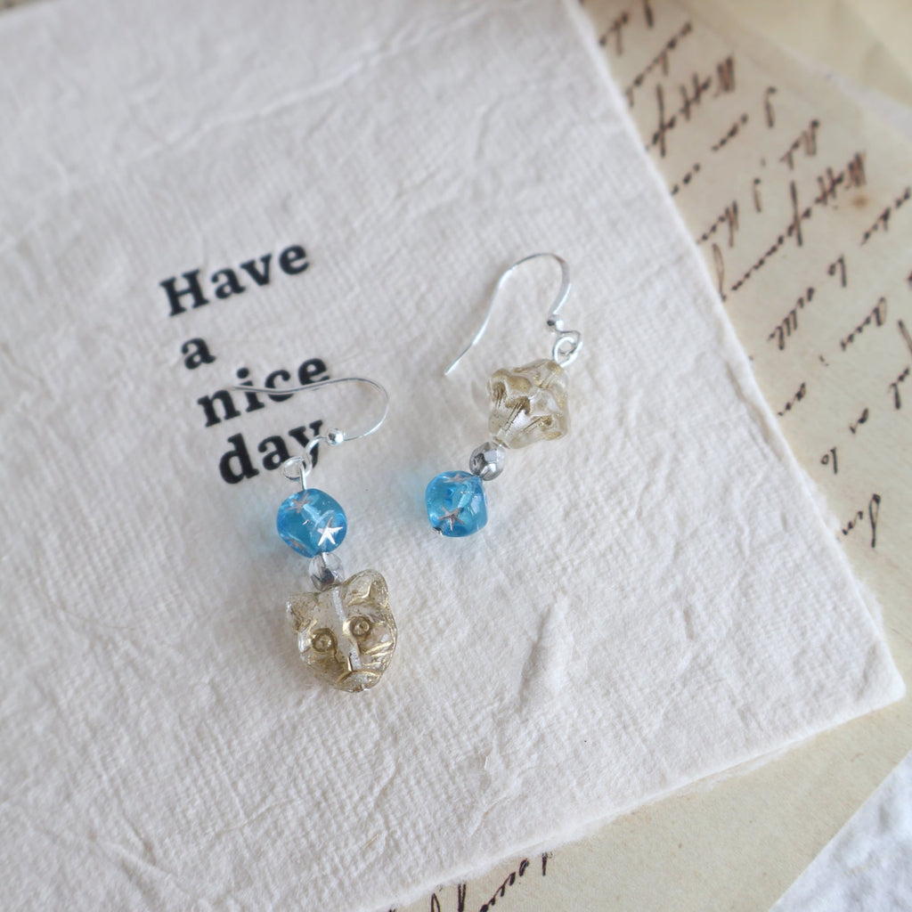 Pair of earrings with blue and clear beads on a textured white surface.