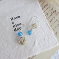 Pair of earrings with blue and clear beads on a textured white surface.