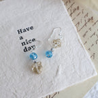 Pair of earrings with blue and clear beads on a textured white surface.