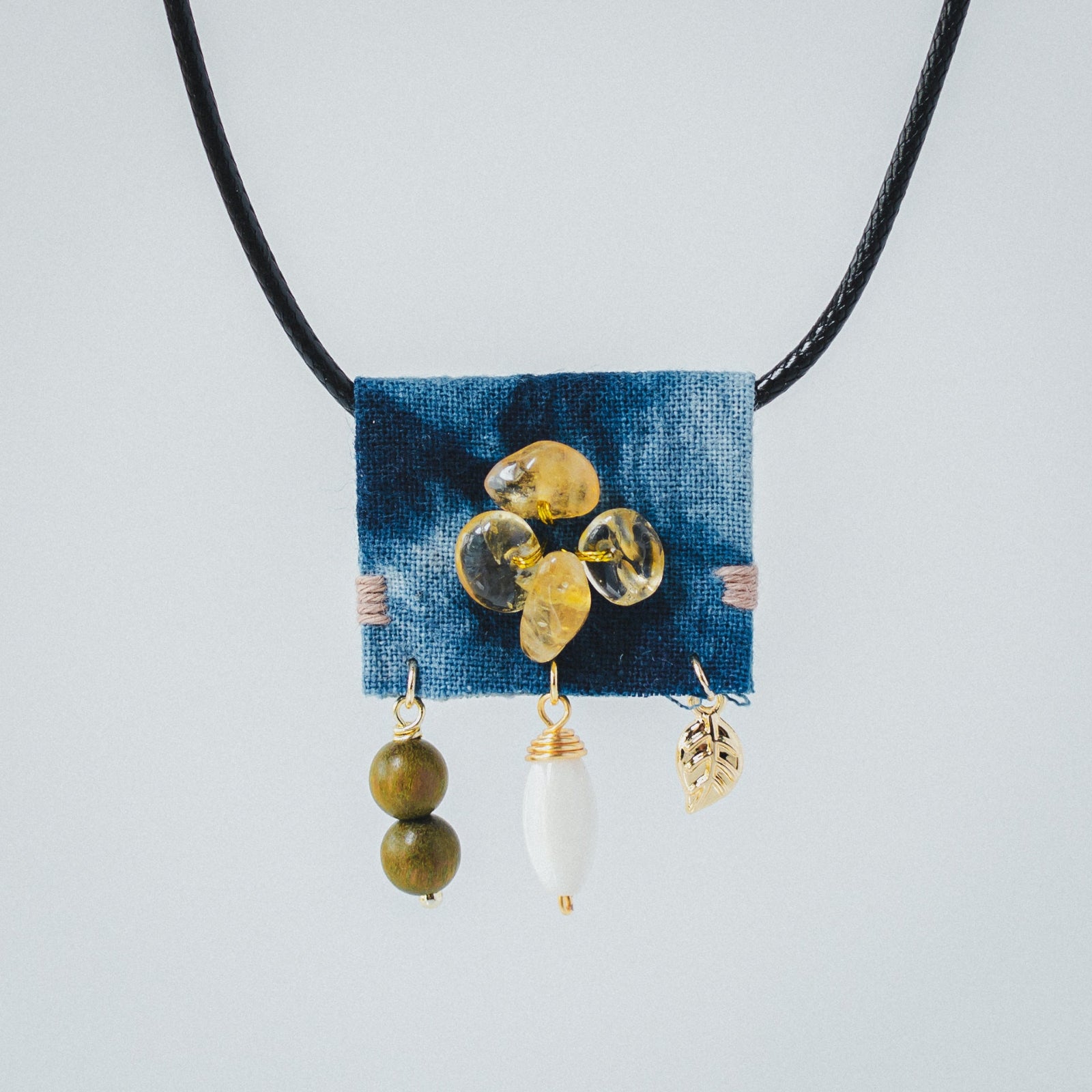 Necklace with blue fabric patch, yellow beads, and gold accents on a light gray background