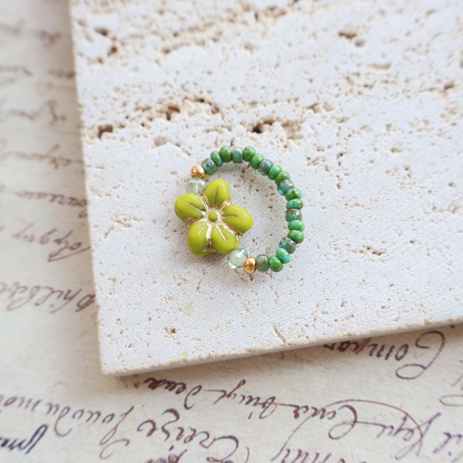 Green beaded ring with a flower-shaped green bead on a textured surface